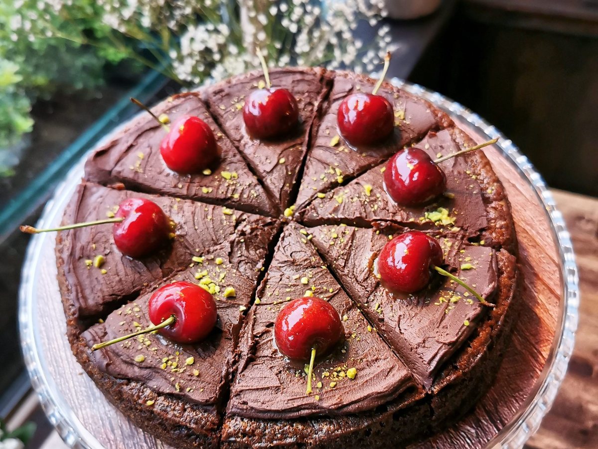 A chocolate cake with cherries and pistachios on a glass stand at Café Nua
